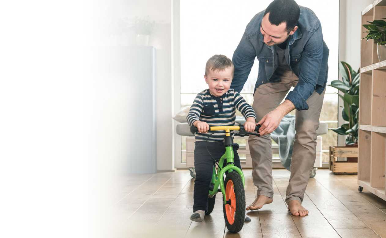 Father guiding son on indoor trainer bicycle on Hardwood Flooring